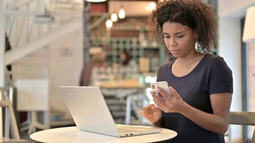 Young African Woman Using Laptop and Smartphone in Cafe