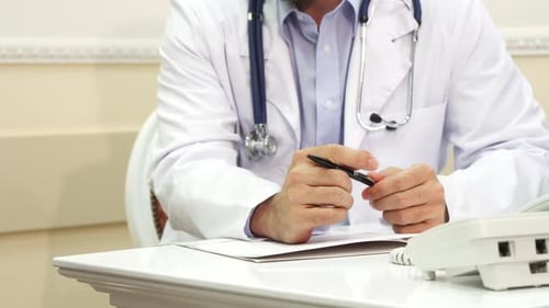 Doctor in White Coat Writing at Desk