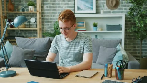 Red-Haired Man Happily Working on Laptop at Home