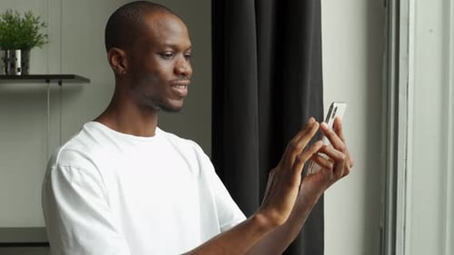 Smiling Man Using Cellphone Indoors by Window