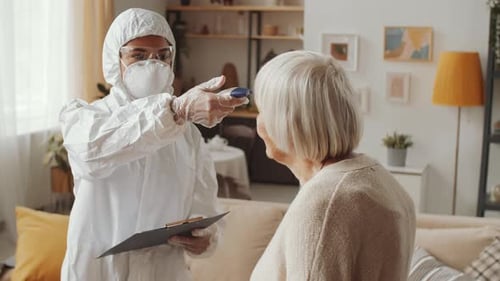 Doctor in Protective Suit Measuring Temperature of Senior Woman