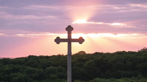 Stone Cross Silhouette at Sunrise Over Green Forest
