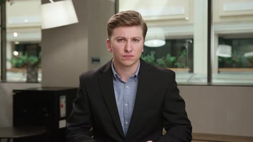 A male office worker communicates on zoom with colleagues at work (look at the camera)