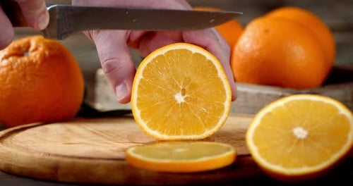 Hand of Man with Knife Cut Ripe Orange Into Round Slices