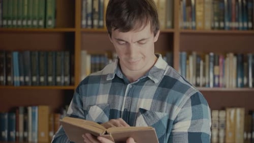 Portrait Shot of the Man Reading a Book Near the Bookshelf in the Library