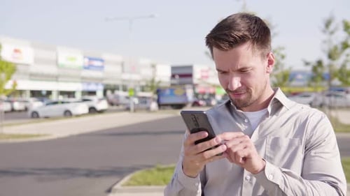 A Young Caucasian Man Takes Selfies with a Smartphone in an Urban Area