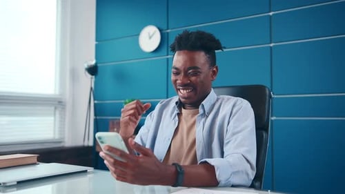 Man Celebrates Success While Looking at Phone in Office