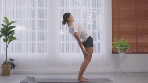 On a yoga mat, an Asian woman does a bridge abduction training
