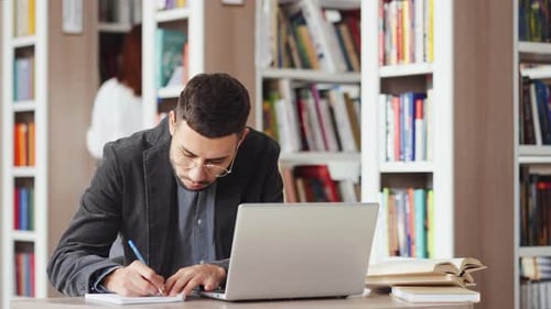 Hombre que usa una computadora portátil para investigar en la biblioteca