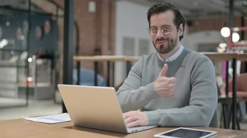 Man Typing on Laptop at Desk Gives Thumbs Up