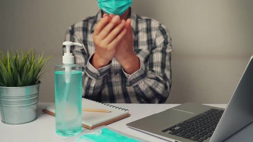 Masked Person Sanitizing Hands, Working on Laptop