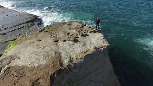Aerial shot of backpacker standing on rock overlooking Pacific Ocean