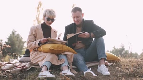 Pareja sentada y leyendo libros de ficción al aire libre en el bosque
