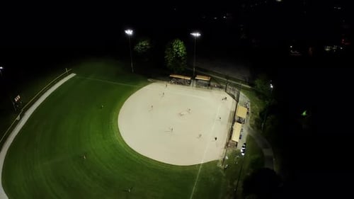 Aerial Drone Footage Of Baseball Field At Night With People Playing Baseball On Grass Field