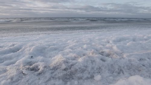 Ice covered sea waves rolling in on beach. Cloudy blue sky and white palette. Rotating panorama gimb