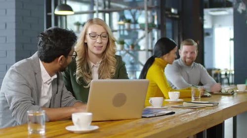 Joyous Diverse Colleagues Chatting and Working on Laptop in Cafe