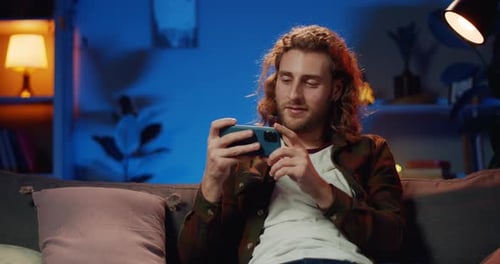 Man Plays Mobile Game at Home at Night