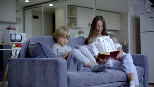 Woman Reading Book, Boy Using Phone on Sofa