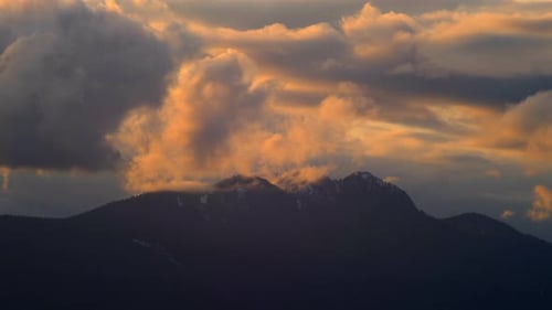 Wolken rollen bei Sonnenuntergang über dem Berggipfel - Zeitraffer