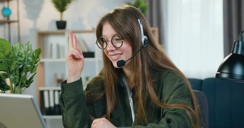 Mujer independiente con auriculares sentada frente a la computadora durante una conferencia en línea