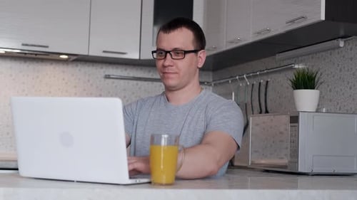 Junger männlicher Freelancer benutzt einen Laptop, während er von zu Hause aus im Internet arbeitet und auf den Bildschirm schaut