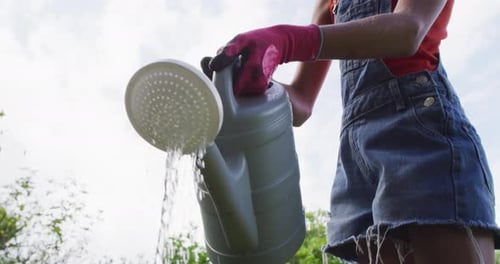 Low angle view of smiling caucasian girl in garden watering plants with watering can