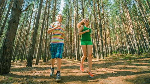Young Adults Running Through a Pine Forest