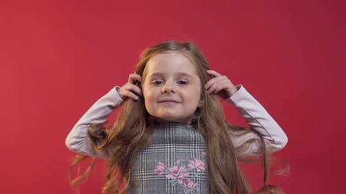 Linda chica de 5 años con pelo largo y rizado posando ante la cámara en el fondo de la pared roja