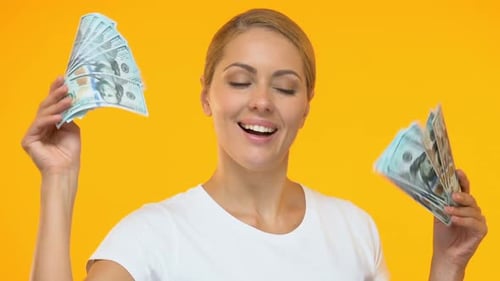 Woman Holds Cash in Front of Yellow Backdrop