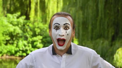 Nahaufnahme eines Pantomimes, der begeistert auf grünem Hintergrund in einem Park in die Kamera blickt. Emotion von