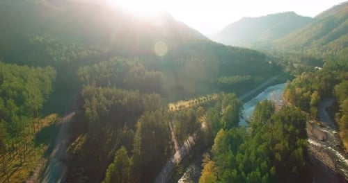 Mid Air Flight Over Fresh Mountain River and Meadow at Sunny Summer Morning. Rural Dirt Road Below.