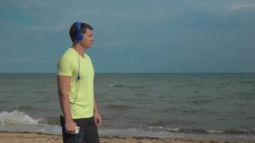 Man Walks Beach with Headphones and Ocean Views