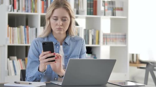 Woman Using Laptop and Phone in Office