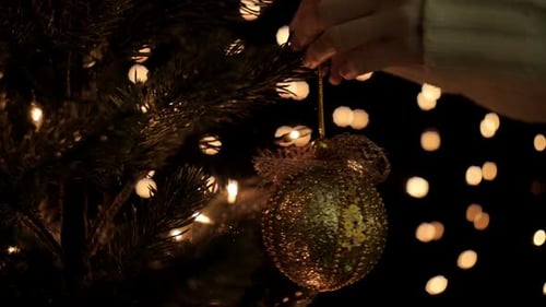 Hands Decorating Christmas Tree with Golden Ornament