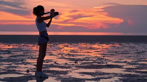 Femme prenant des photos du coucher de soleil sur la plage