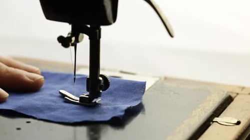 Mann näht blauen Stoff auf einer Vintage-Nähmaschine auf hellem Hintergrund