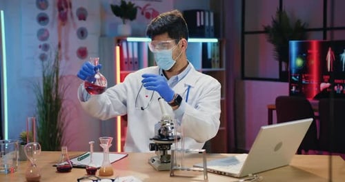Químico con máscara protectora y uniforme que trabaja con líquidos químicos en un laboratorio nocturno