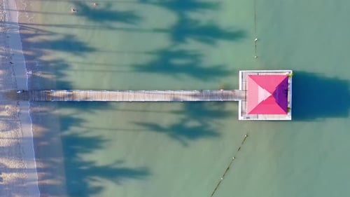 Jetty with gazebo in ocean, exotic beachfront with palms; overhead aerial riser