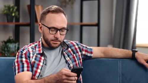 Man With Glasses Using Smartphone on Couch Indoors