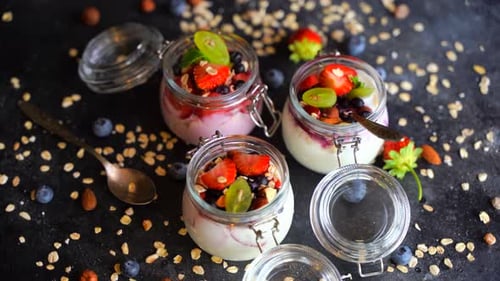 Yogurt Oat Muesli and Fresh Berries in Jars Rotate on a Dark Background