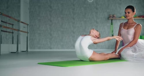 Joven maestra ayuda a una bailarina preadolescente a hacer backbend en el estudio