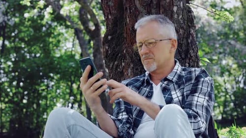 Man Using Smartphone While Relaxing by Tree