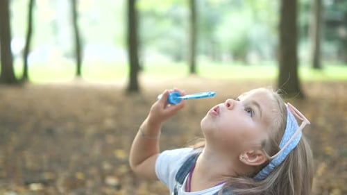 Little happy child girl blowing soap bubbles outside in green park. Outdoor summer activities