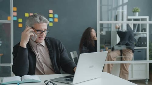 Man Speaking on Phone While Using Laptop