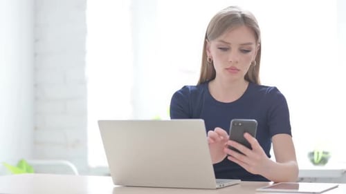 Young Woman Uses Laptop and Smartphone