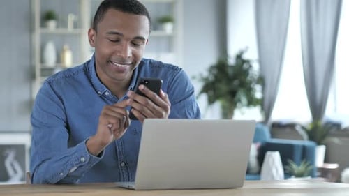 Man Uses Smartphone and Laptop in Home Office