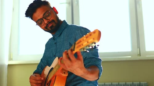 Man Playing Acoustic Guitar Indoors in Bright Sunlight