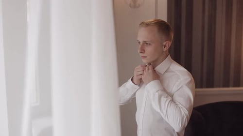 Young Man Buttoning Up White Shirt Indoors