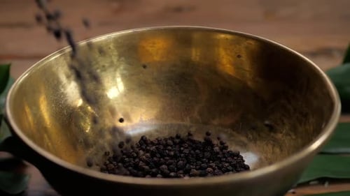 Black Peppercorns Being Poured Into a Gold Bowl