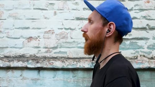 Portrait d'un jeune homme barbu rouge en t-shirt noir et snapback dans un style rock sur fond urbain